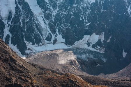 High mountain wall with snow and sunlit cracked glacier in mountain cirque close-up. Crevasses on glacier in sunlight. Nature background of snow mountains. Fading autumn colors on rocks in mountains.の写真素材