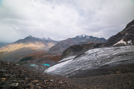 Top view from glacier to small turquoise lakes and pyramid shaped mountain. Beautiful lakes among fading autumn colors and high mountain range. Sharp peak in sunlight and shadows of clouds.の写真素材