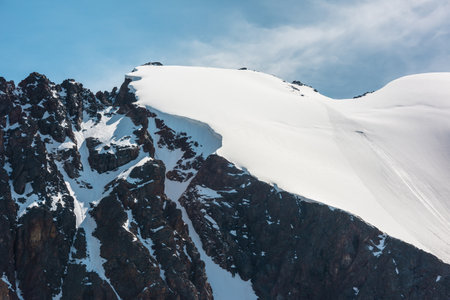 Minimalist alpine landscape with snow-covered mountain top and sharp rocks in sunlight. Simple minimalism with snowbound mountain in blue sky. Minimal view to snow mountain peak at very high altitude.の写真素材