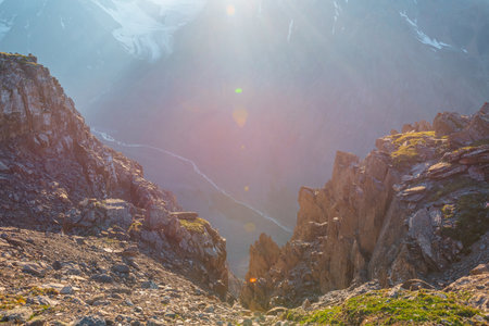 Sunny mountain view from cliff at very high altitude. Scenic alpine landscape with beautiful sharp rocks and couloirs and large glacier in sunlight. Beautiful scenery on abyss edge with sharp stones.の写真素材