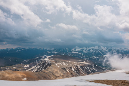 Awesome top view through clouds to high snowy mountains. Scenic landscape with beautiful snow mountains in low clouds. Atmospheric alpine view from stone hill to snow mountain range with low clouds.の写真素材