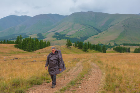 Satisfied tourist returns from mountains in overcast. Happy man in raincoat walks through hills and forest in bad weather. Traveler goes towards adventure. Hiker and mountain range under cloudy sky.の写真素材