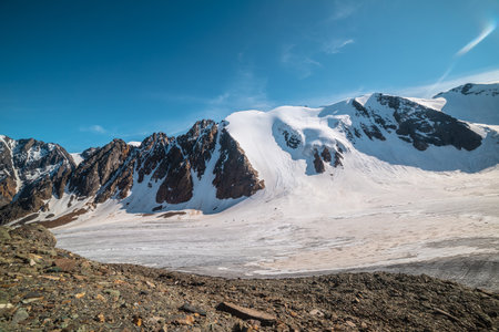 Scenic mountain landscape with large glacier in sunlight. Awesome snowy scenery with glacial tongue under cirrus clouds. Beautiful alpine view to snow mountain tops at very high altitude in sunny day.の写真素材