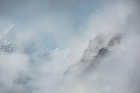 Lovely scenery with big snowy mountains in thick clouds. High mountain wall in gantly cloudy sky. Scenic view to large snow mountain in clearance of dense fog. Beautiful diagonal rocks in low clouds.の写真素材