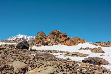 Scenic mountain landscape with old rocks and stones among snow in sunlight. Alpine scenery with stone outliers on high mountain under blue sky in sunny day. Sharp rocks at very high altitude.の写真素材
