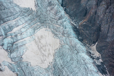 Beautiful mountain landscape with vertical glacier tongue with cracks among rocks. Awesome natural backdrop of large glacier with icefall. Nature texture of mountain glacier with fissures close up.の写真素材