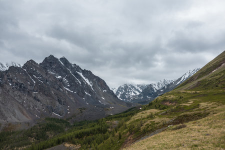 Dark atmospheric landscape with large mountain top under gray cloudy sky. Gloomy aerial view to high snowy mountain range with sharp rocks in low clouds.の写真素材