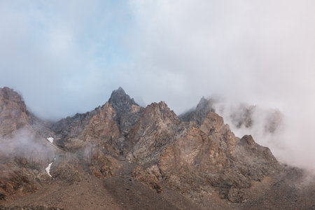 Scenic alpine landscape with rocky mountains in dense low clouds in morning sunlight. Colorful mountain scenery with sharp rocks among thick low clouds. Awesome view to high rockies in low cloudiness.の写真素材