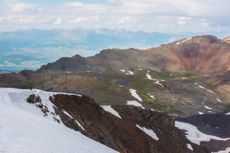 Awesome alpine view from sharp rocks with snow cornice to sunlit multicolor mountain valley. Scenic top view from stone hill to motley high mountains at very high altitude. Colorful mountain landscapeの写真素材