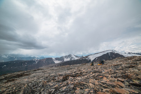 Two big backpacks among sharp stones on high stony mountain pass with view to large mountain range...