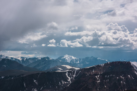 Dark atmospheric landscape with mountain silhouettes and large snow-capped peaked top under rainy clouds. Dramatic alpine view to high mountains in gray cloudy sky. Big snowy mountain range in rain.の写真素材