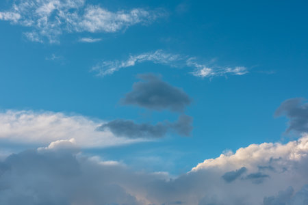 Scenic view to dark gray rainy cloud in center among light clouds in blue sky. Nature background of dramatic cloudy sky. Beautiful skyscape in changeable weather. Nature texture of sunset cloudy skiesの写真素材