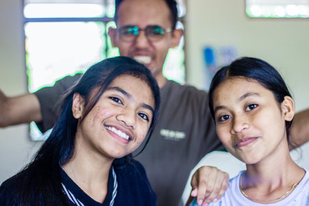 Muntilan, Indonesia - 2 Apr 2026: Two happy Asian teenage girls smiling with a playful man blurred in the background. Student life and education friendship conceptのeditorial素材