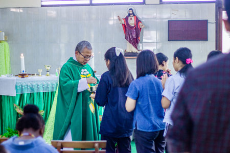 Muntilan, Indonesia - 5 Apr 2026: Catholic priest in green vestments distributing Holy Communion to...