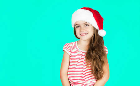 Little bright beautiful girl emotionally posing in Santa hat on an isolated turquoise backgroundの写真素材