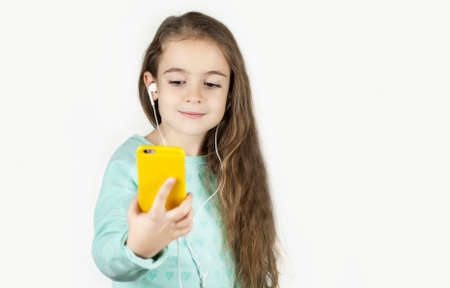 Bright beautiful little girl in headphones with a phone in her hands emotionally talks and rejoices...