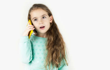 Bright beautiful little girl in headphones with the phone is emotionally surprised on an isolated...