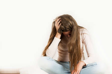 A very sad offended emotional girl is sitting with her head down on an isolated background.の写真素材