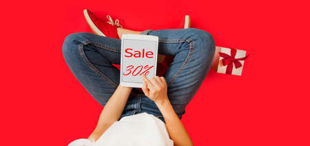 girl with tablet in her hands, gifts, discounts, sitting on an isolated red background, Lovers day concept,Valentine's Day.の写真素材