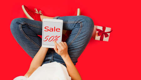 girl with tablet in her hands, gifts, discounts, sitting on an isolated red background, Lovers day concept,Valentine's Day.の写真素材