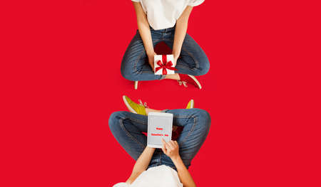 girl with white gift with a red bow is sitting on an isolated red background. Lovers day concept,Valentine's Day.の写真素材
