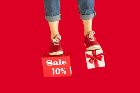 feet with a gift for the holidays on an isolated red background, a girl with a gift, giving gifts,...