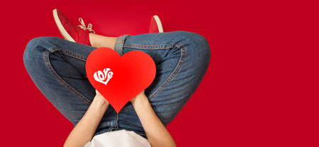 legs of a girl with a red heart in her hands sitting on an isolated red background. Lovers day concept,Valentine's Day.の写真素材