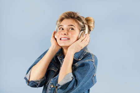 Charming young beautiful girl in headphones sings and dances in the studio on an isolated blue background. Concept of happiness of musical lifeの写真素材
