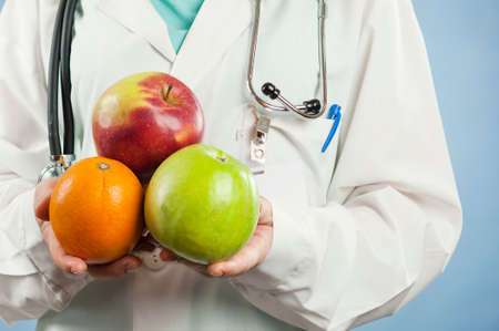 Young beautiful girl doctor nutritionist with fruit in hand on blue isolated background. Healthy eating conceptの写真素材