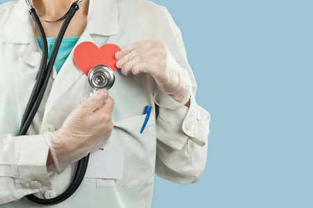 Young beautiful girl doctor with a red heart in her hands on a blue isolated background.Concept of...