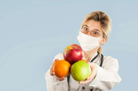 Young beautiful girl doctor nutritionist with fruit in hand on blue isolated background. Healthy eating conceptの写真素材