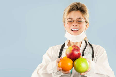 Young beautiful girl doctor nutritionist with fruit in hand on blue isolated background. Healthy...