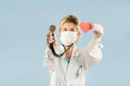 Young beautiful girl doctor with a red heart in her hands on a blue isolated background.Concept of loveの写真素材