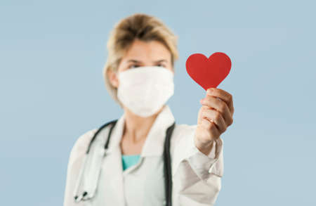 Young beautiful girl doctor with a red heart in her hands on a blue isolated background.Concept of loveの写真素材