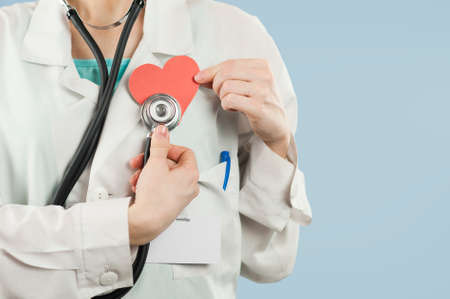 Young beautiful girl doctor with a red heart in her hands on a blue isolated background.Concept of loveの写真素材