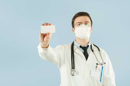 Doctor holding copy space. Close-up of a confident young doctor showing his business card and smiling while standing against backgroundの写真素材