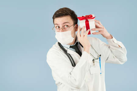 young doctor student with a gift in his hands on an isolated blue background.concept medicine and health, holidays and giftsの写真素材