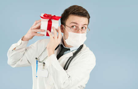 young doctor student with a gift in his hands on an isolated blue background.concept medicine and health, holidays and giftsの写真素材