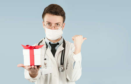 young doctor student with a gift in his hands on an isolated blue background.concept medicine and health, holidays and giftsの写真素材