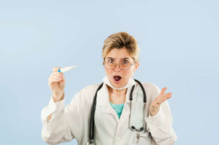 Young beautiful girl doctor student with thermometer in hands on a blue isolated backgroundの写真素材