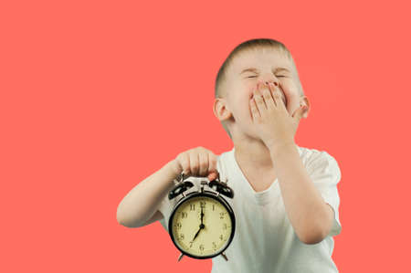 a beautiful child boy with an alarm clock in his hands early in the morning ziva and does not want...