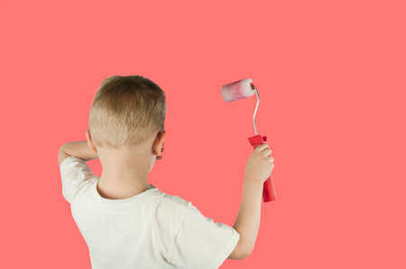 Beautiful blond child boy paints the wall with a roller and writes paint on the wall on an isolated...