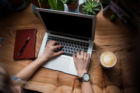 A girl in a cafe with a laptop does work in a cozy place with a cup of coffee, gets pleasure. The concept of freelancing and working in pleasureの写真素材