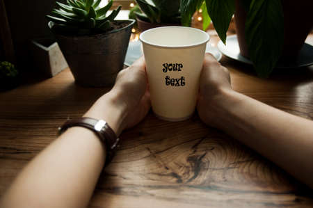 girl holds hot coffee in her hands against the background of a beautiful wooden window sill. A cozy...