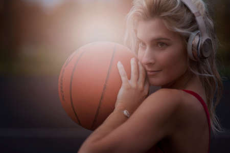 Portrait of a gorgeous woman outdoors posing while listening to music with headphones holding a basketballの写真素材