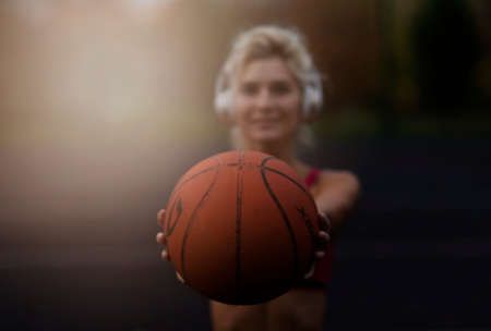 Portrait of a athletic woman outdoors posing while listening to music with headphones holding a basketballの写真素材
