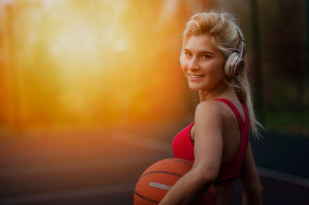 Portrait of a athletic woman outdoors posing while listening to music with headphones holding a...