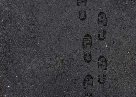 Black wet footprints over gray pedestrian asphalt roadの写真素材