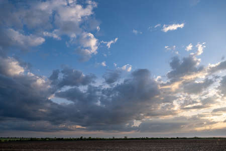 A picturesque sunset over an agricultural field. Blue sky and the sun behind beautiful clouds at...