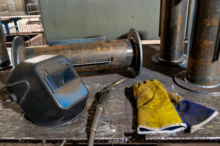 Welder's workplace, welding equipment on a steel table with a welding mask, leather gloves, welding torch and weldable products. working environment. high quality photoの写真素材